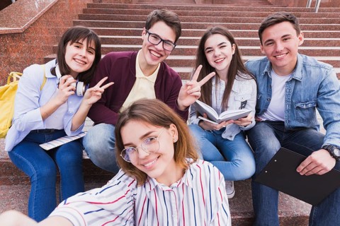 Students sitting stairs gesturing two fingers looking camera