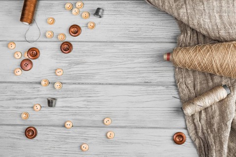 Top view button string spool needle thimble cloth wooden background