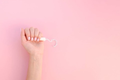Top view hand holding tampon pink background