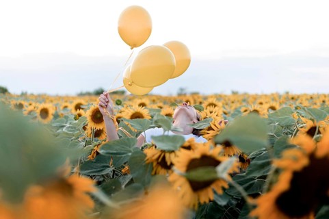 Woman holding balloons sunflower field