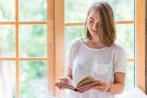 Woman standing front window reading book