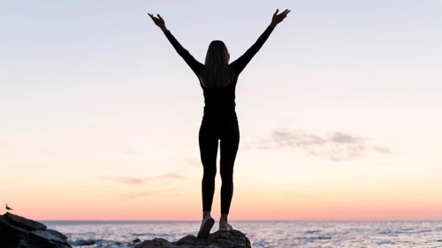 Back view woman standing coast with her arms up