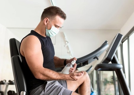 Side view man with medical mask using hand sanitizer gym