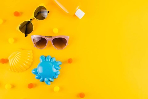 Overhead view sunglasses sunscreen lotion bottle scallop crab toy yellow backdrop