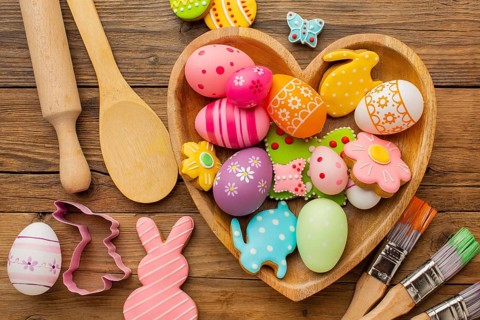 Top view colorful easter eggs heart shaped plate with kitchen utensils paint brushes