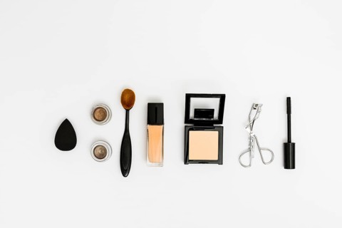 Overhead view blender eyeshadow oval brush compact powder eyelash curler mascara brush white backdrop