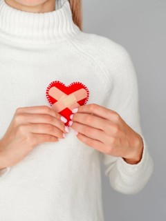 Woman holding heart with band aids