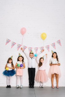 Birthday boy standing with girls against white wall decorated with bunting