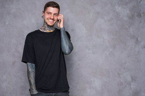 Smiling portrait tattooed young man with pierced ears talking mobile phone