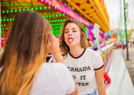 Rear view woman taking her friend showing tongue amusement park