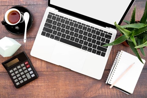 Open laptop with coffee cup spiral notebook calculator paper house model aloe vera plants wooden table