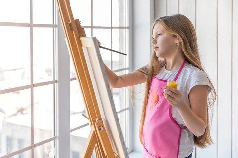 Side view girl holding yellow paint bottle hand painting easel with paintbrush