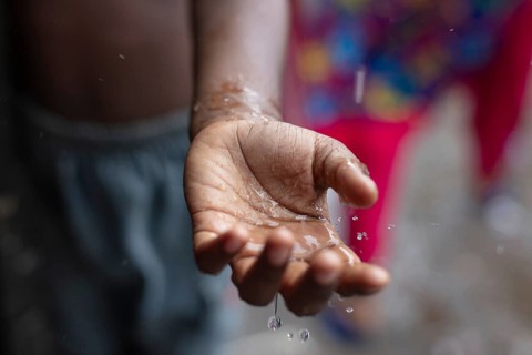 Drops of water fall on the palm of a boy's hand during a monsoon downpour