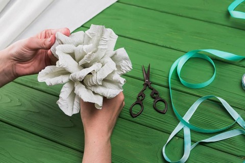 Person s hand holding fake crepe paper flower green textured background
