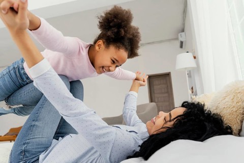 Mother playing with her smiley daughter bed home