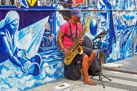 Busker playing saxophone in front of mural in the city centre of capital Montevideo