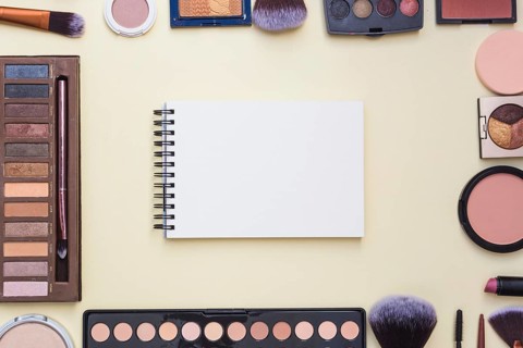 Overhead view spiral blank notepad surrounded with cosmetics product