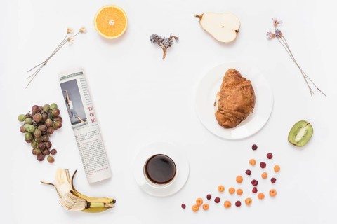 Rolled up newspaper with coffee cup croissant fruits white background