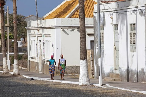 Local Creole women walking in street along white colonial buildings of the town Tarrafal on the island Santiago