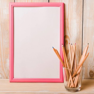 White blank frame with pink border colored pencils glass holder wooden desk