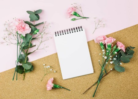 Overhead view spiral notepad surrounded with gypsophila carnation flowers dual pink cardboard background
