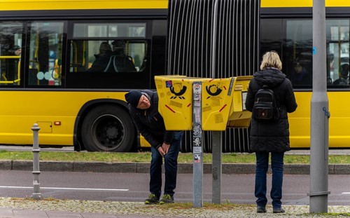 Tourists marvelling at and examining a yellow letterbox by the roadside