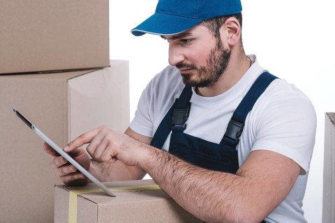 Serious courier browsing tablet near parcels