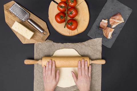 Hand rolling pizza dough parchment paper with pizza ingredient black background