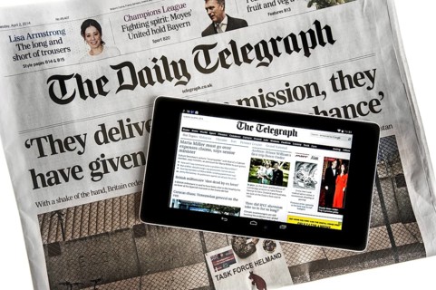 Touchscreen digital tablet showing online news on top of British The Daily Telegraph newspaper on white background