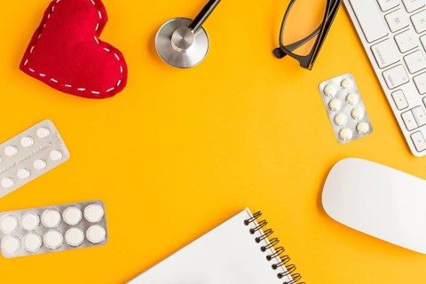 Arrangement blister packed medicines stitched heart shape spiral notepad wireless keyboard mouse spectacles stethoscope yellow backdrop
