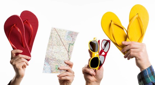 Hand holding travel items with flip flops sunglasses