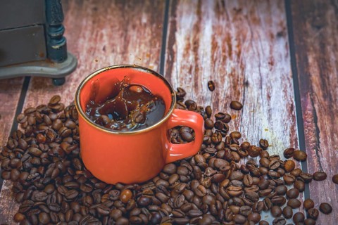 Red coffee mug with coffee beans falling inside with splash effect splash in the background a manual coffee grinder