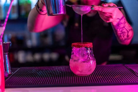 Close-up of a bartender preparing a cocktail with mixer and strain