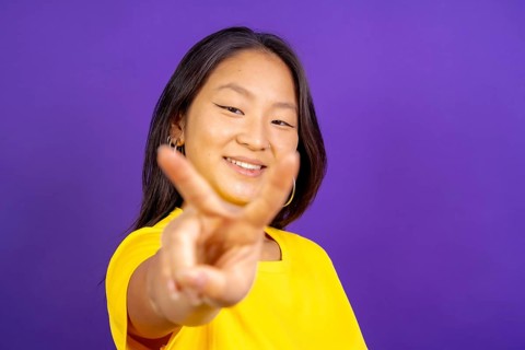 Studio photo with purple background of a chinese woman gesturing victory smiling at camera