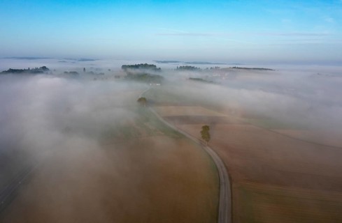 Drone view of a rural landscape shrouded in dense morning fog with a country road near Prambachkirchen