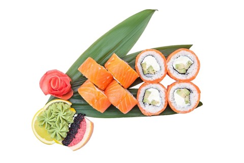 Overhead view of sushi roll with raw salmon fillet on top with avocado served on bamboo leaves