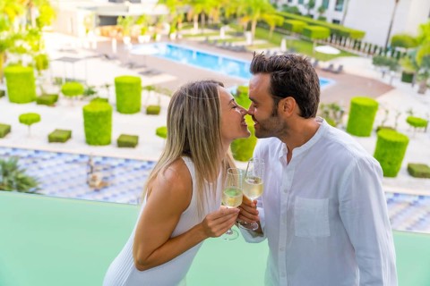 Newlywed couple kissing while toasting with champagne in the terrace of a luxury hotel