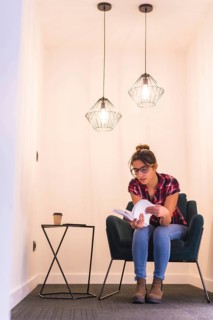 Vertical portrait of a young woman reading a book at home in a cozy corner of a room