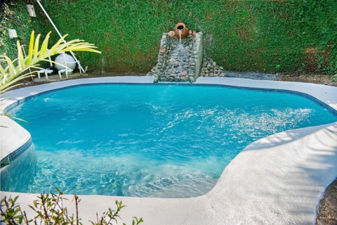 Swimming pool designs for the home. Crystal water home pool surrounded by a garden. Home swimming pool maintenance concept. Homemade swimming pool in a garden