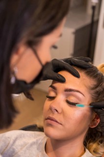 Vertical photo of a professional applying mascara to the eyelashes of the beautiful woman in the beauty salon