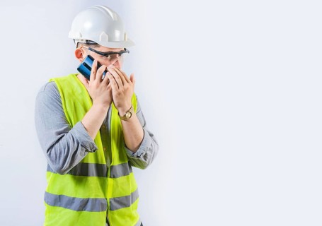 Male engineer talking on the phone secretly isolated. Young engineer in helmet talking on cell phone in silence