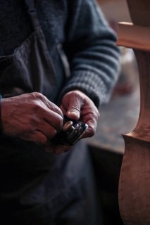 Senior violinmaker wrinkled old hands holding a tool chisel in workshop in Cremona