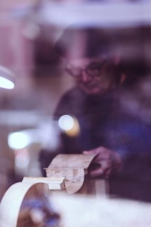 Senior expert luthier artisan violin maker carve sculpt chisel ribs of a new classical model cello in workshop Cremona Italy