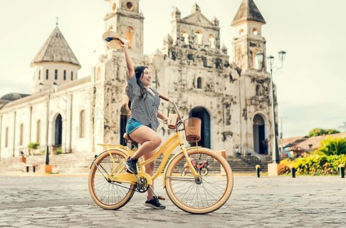 Lifestyle of a happy girl riding a bicycle holding her hat on the street. Happy young woman in hat riding a bicycle on the street. Granada