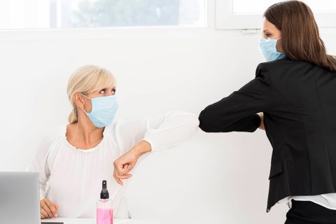 Coworkers wearing masks elbow bump each other