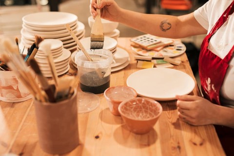 Female taking ceramic color paint plate with brush