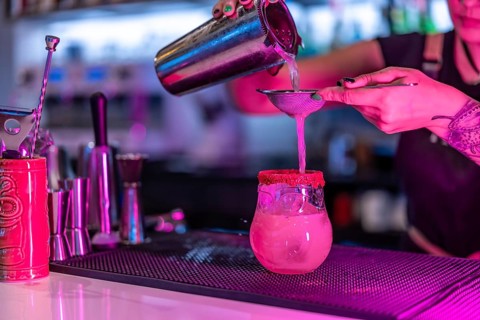 Cropped close-up photo of a woman mixing ingredients of a cocktail in the counter of a nightclub