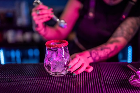 Close-up of a bartender preparing a margarita cocktail adding ice in the counter of a bar with neon lights
