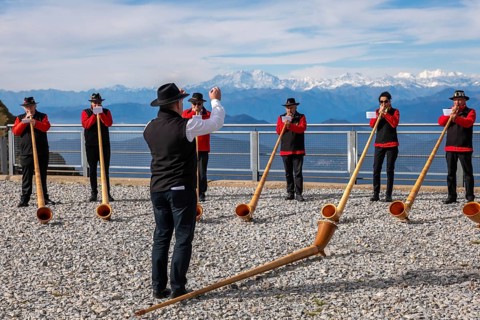 Group of Musicians Playing on Horns of the Alps with Mountainscape and View over Snow Capped Monte Rosa in a Sunny Day in Monte Generoso