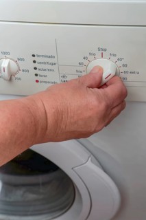 Woman hand choosing program on automatic washing machine for laundry at home. Turning knob on control panel